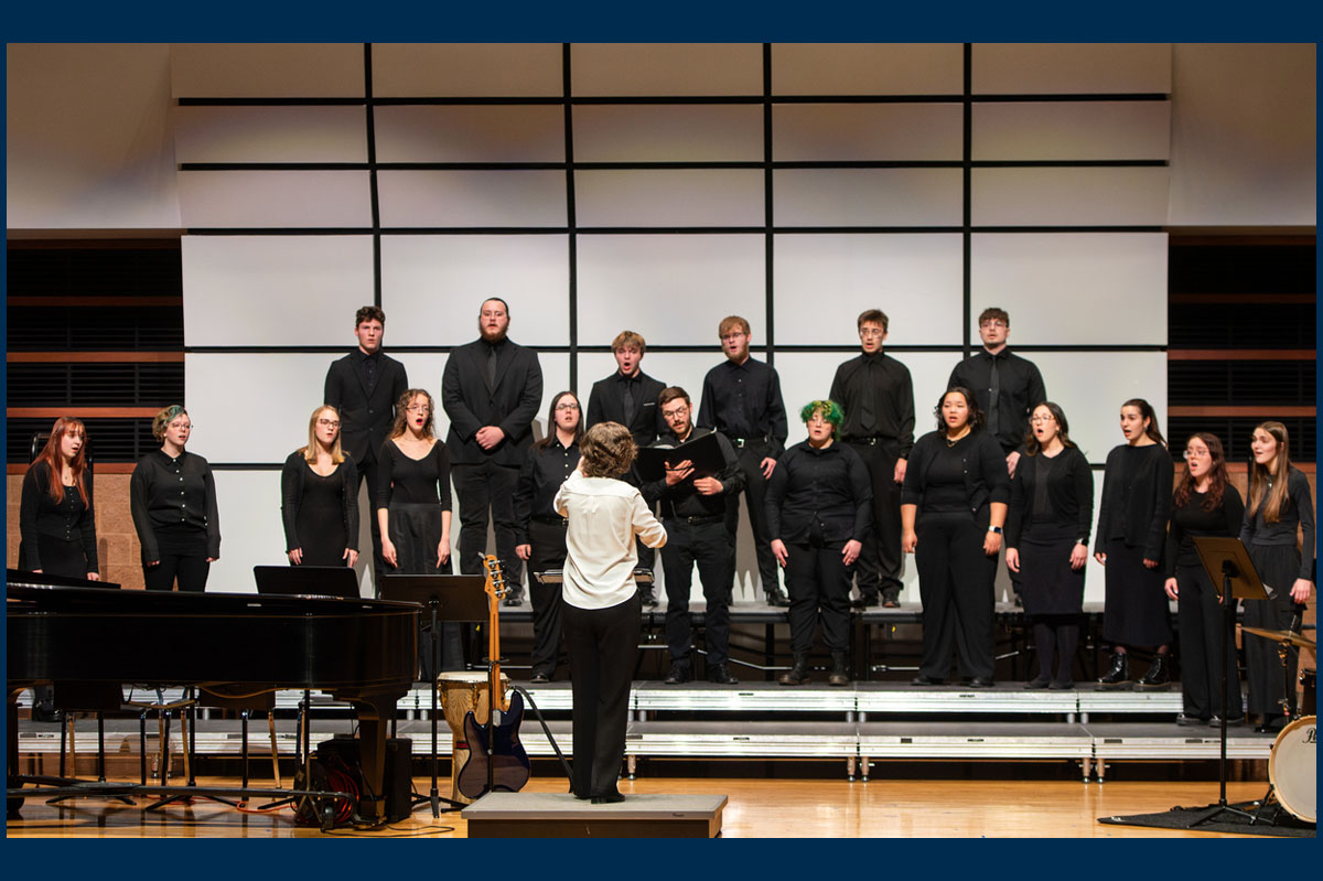 woman in white shirt conducting singers in dark suits